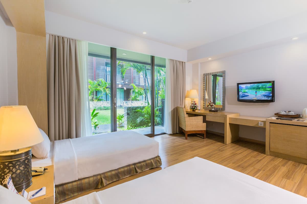 A hotel room with a bed, desk, TV, and large windows overlooking a garden.
