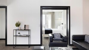Une chambre d’hôtel moderne avec un canapé en cuir noir, un tapis à motifs noir et blanc et une bibliothèque agrémentée d’objets décoratifs.