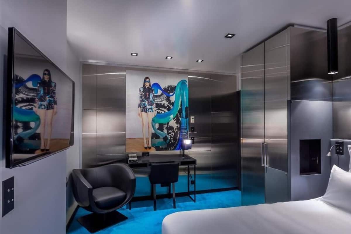 Une chambre d’hôtel moderne équipée d’un lit, d’un bureau, d’une chaise et d’un grand miroir.