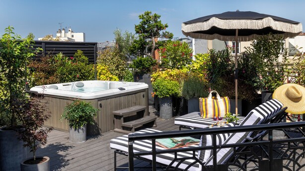Une terrasse sur le toit équipée d’un jacuzzi, de chaises longues et d’un parasol.