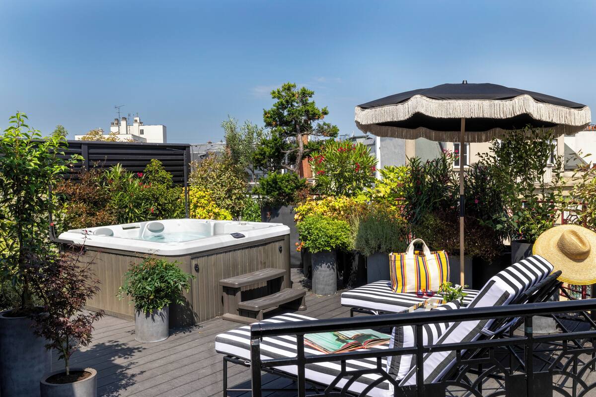 Une terrasse sur le toit équipée d’un jacuzzi, de chaises longues et d’un parasol.