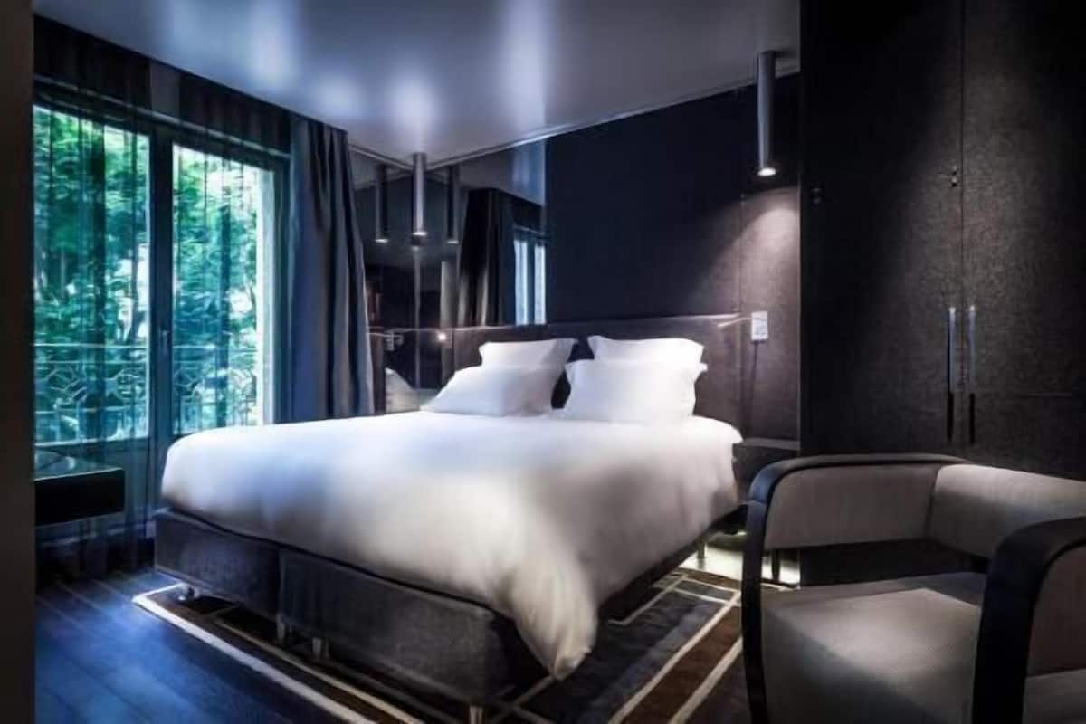 Une chambre moderne avec un grand lit, une chaise et une vue sur la verdure par la fenêtre.