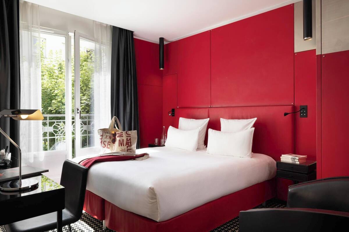 Une chambre d’hôtel avec un grand lit, un bureau avec une lampe, une chaise et une vue sur la verdure par la fenêtre.
