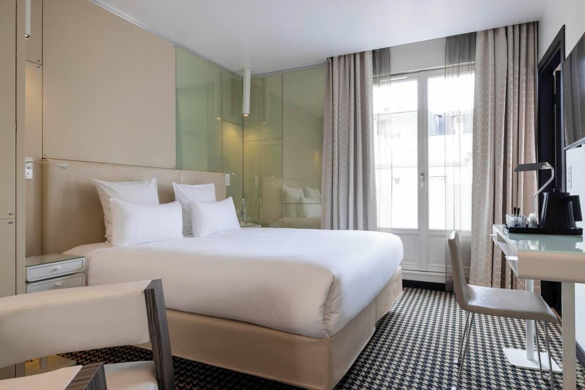 Une chambre d’hôtel comprenant un lit, une table de chevet, une chaise et un bureau avec une autre chaise.