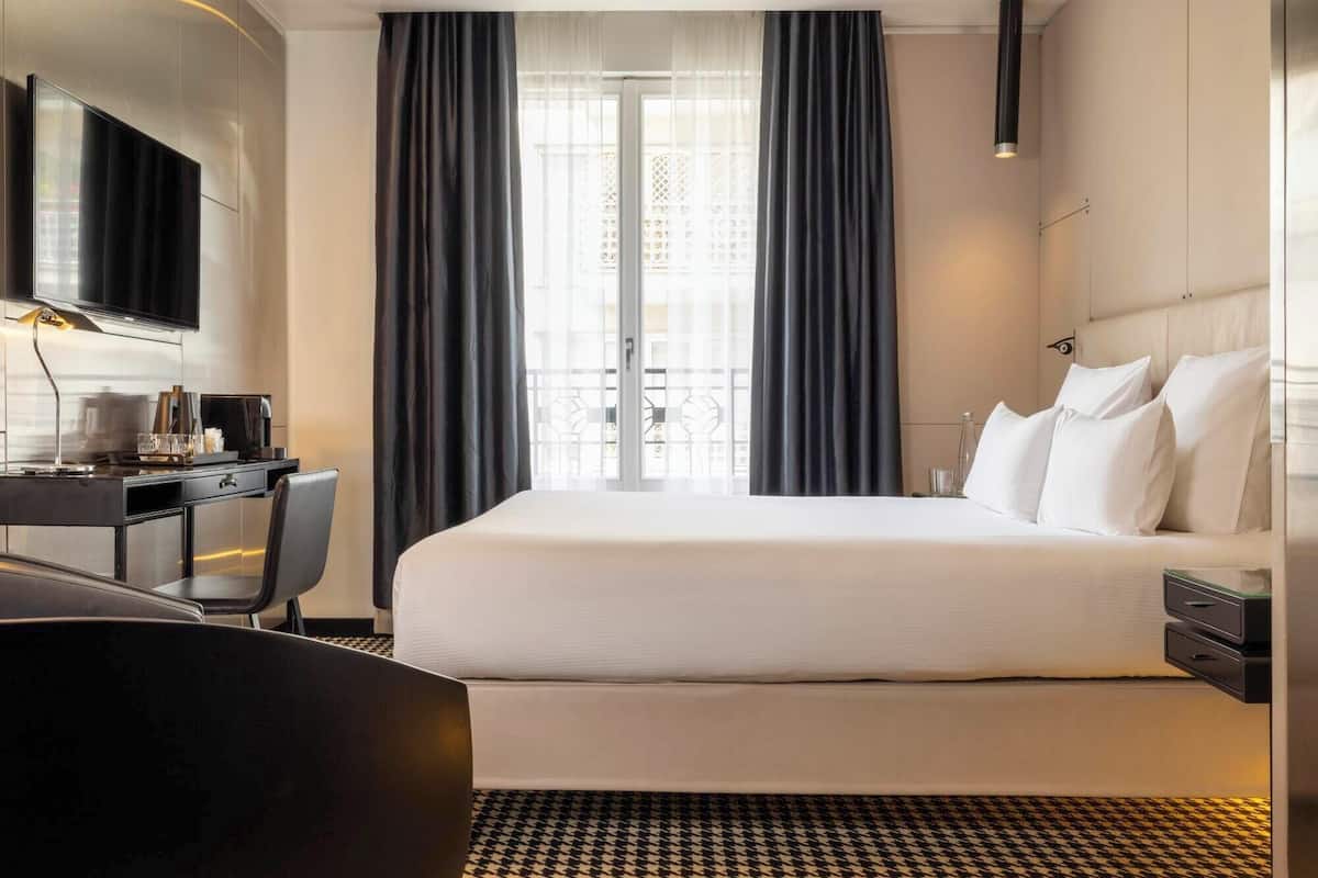 Une chambre d’hôtel avec un lit, un bureau et une chaise, une télévision et une fenêtre avec des rideaux.