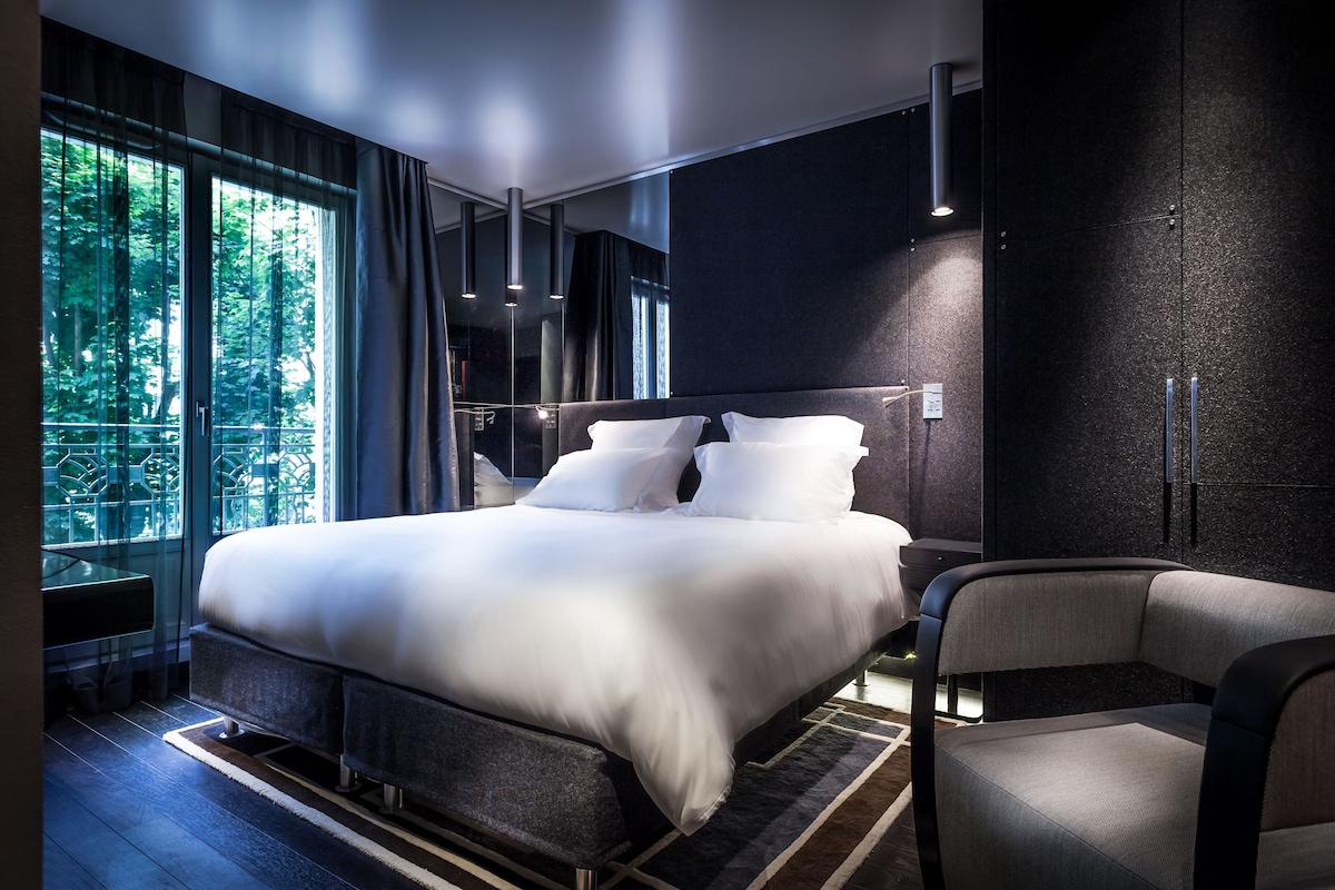 A modern bedroom with a large bed, a chair, and a view of trees through the window.