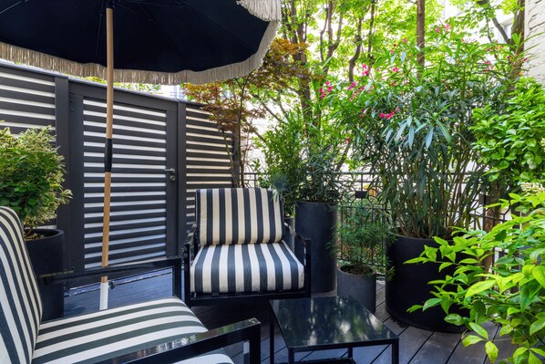 A patio area with striped chairs, a table, and a black umbrella. - Félicien & SPA (Paris)