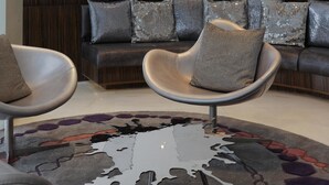 Een moderne zithoek met een hoekbank, twee fauteuils en een vloerkleed met dessin.