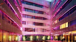 Een modern gebouw met meerdere verdiepingen, grote ramen en een centrale binnenplaats met een reflecterend oppervlak.