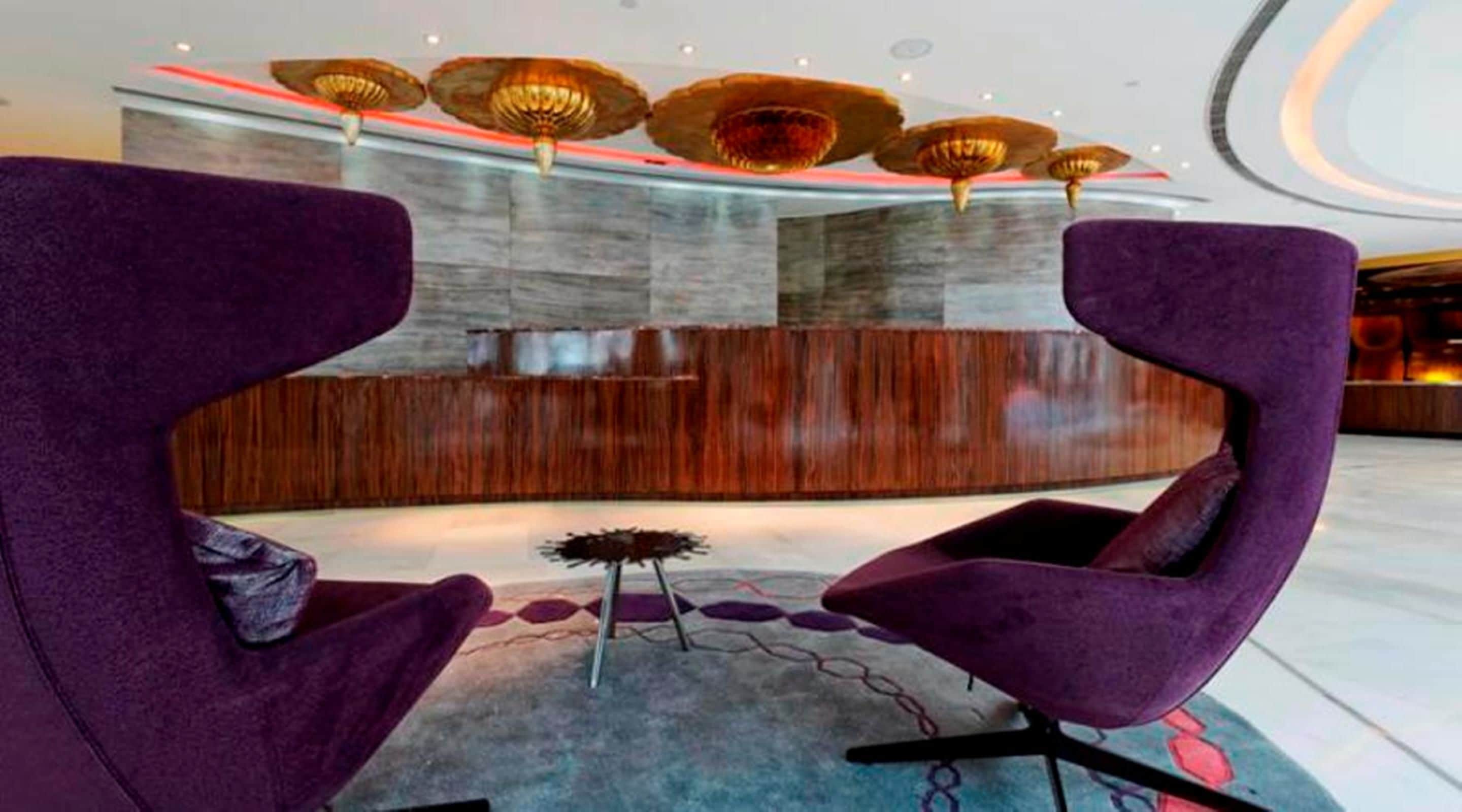 A reception area with a modern design, featuring a wooden reception desk, purple seating, and unique ceiling lighting.