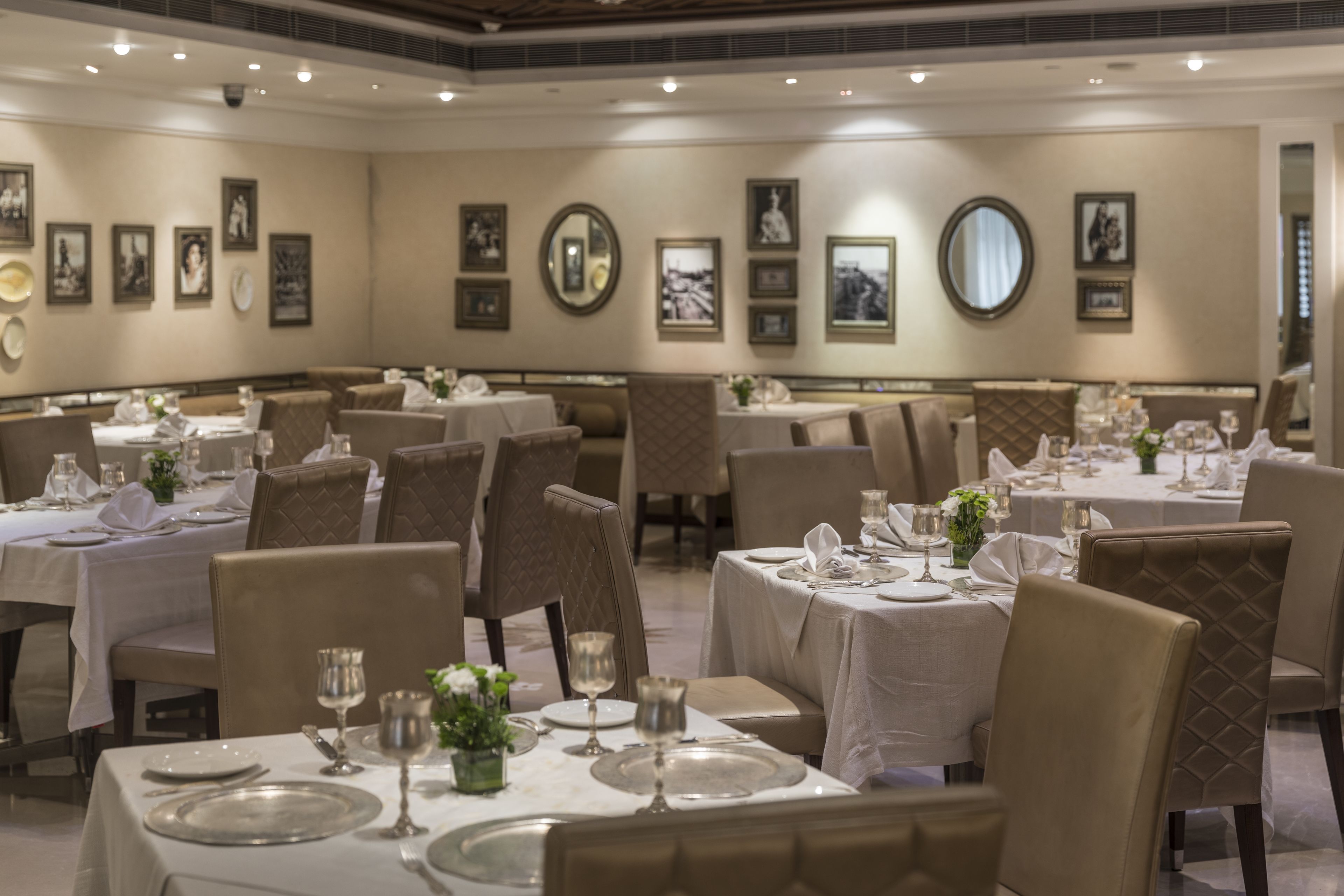 A dining area with tables set for a meal, chairs, and framed pictures on the walls.