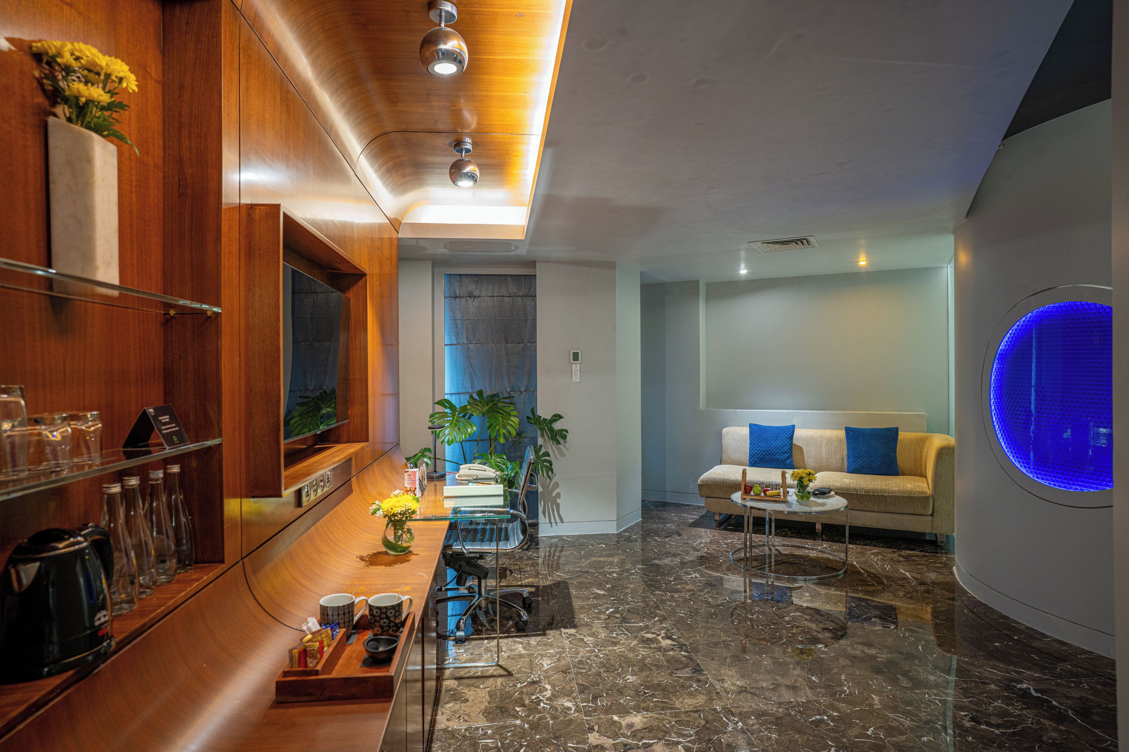 Un intérieur moderne avec un comptoir d’accueil en bois, un espace détente comprenant un canapé et une table basse, et un élément décoratif circulaire illuminé de lumière bleue sur le mur.