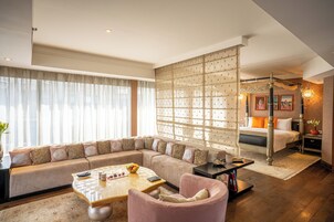 Habitación de hotel moderna con un sofá grande, un área de estar separada, una cama con un cabecero decorado y un panel decorativo en la pared.