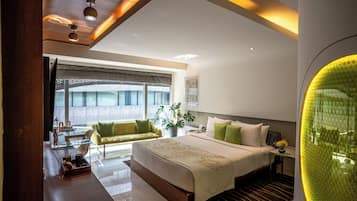 A modern hotel room with a large bed, a sitting area with a sofa, and a dining table.