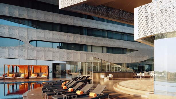 Een modern hotel met een zwembadgedeelte, inclusief ligbedden en een bar met glazen wanden.