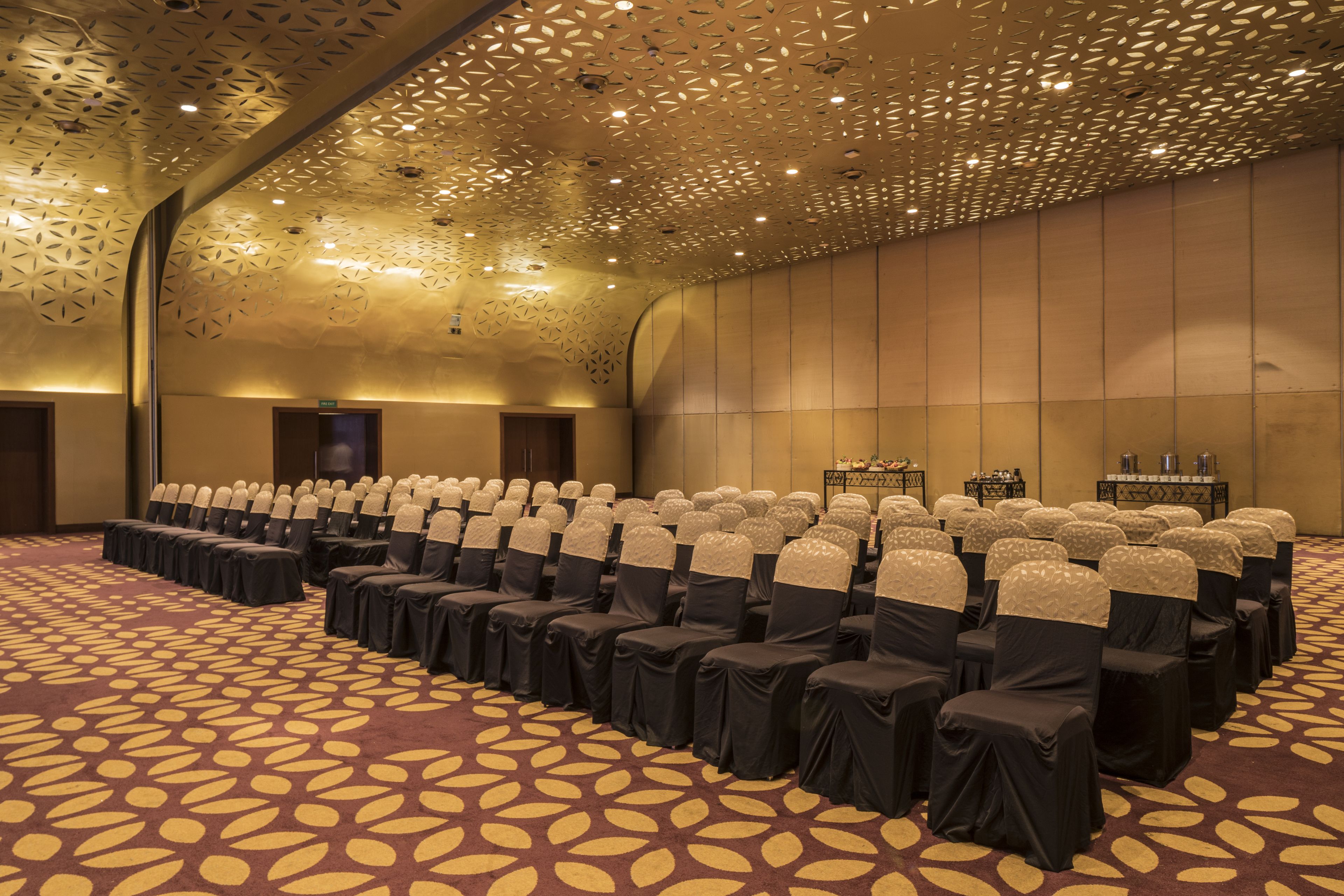 Un salón de conferencias con filas de sillas, una alfombra estampada y un techo decorativo.
