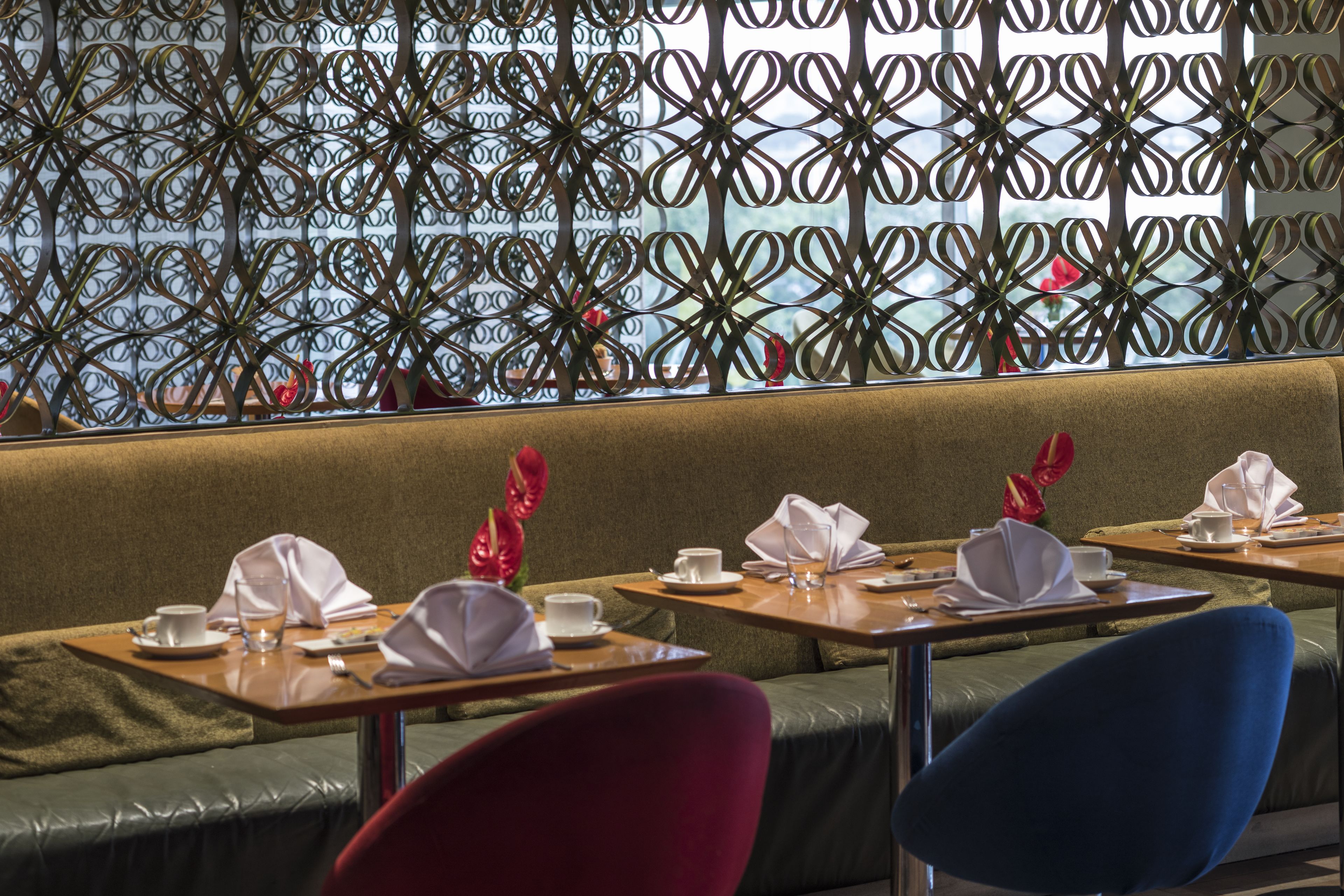 En restaurant med et grønt polstret bænkarrangement, borde med hvidt service og en dekorativ metaladskillelse.