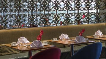 En restaurant med et grønt polstret bænkarrangement, borde med hvidt service og en dekorativ metaladskillelse.