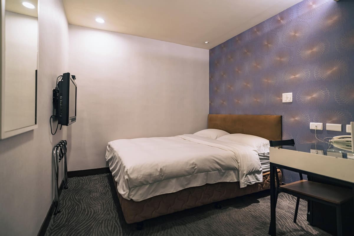 A hotel room with a bed, a desk, a telephone, and a wall-mounted heater.