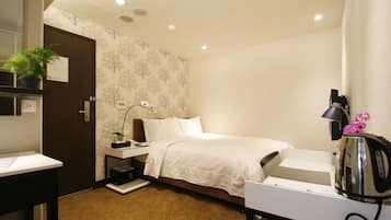 Een hotelkamer met een bed, nachtkastje, lamp en een waterkoker.