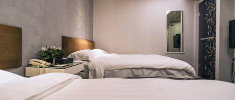 A hotel room with two beds, a bedside table with a phone and a plant, a mirror, and a TV mounted on the wall.