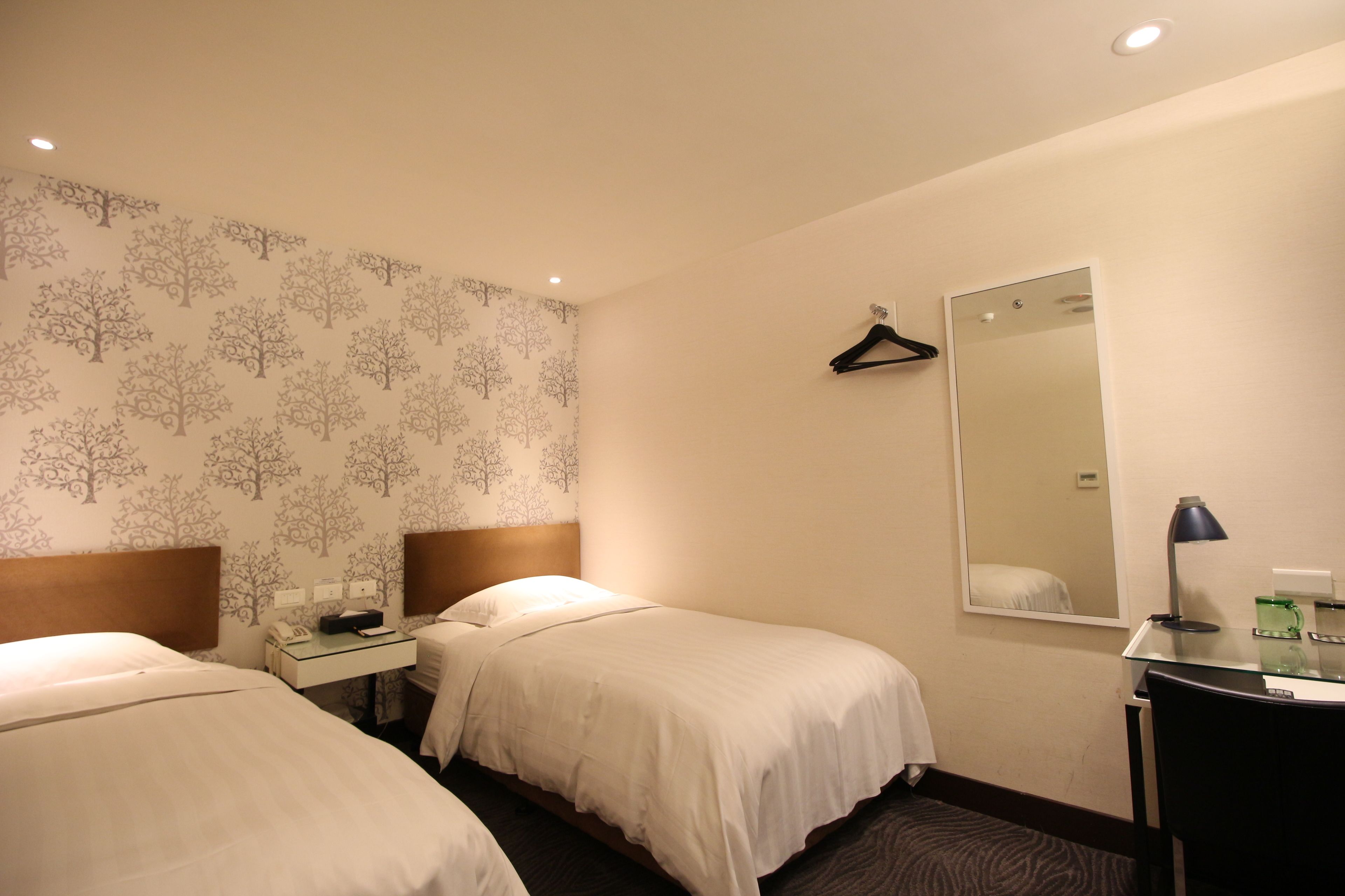 A hotel room with two beds, a desk with a telephone and a lamp, a mirror, and a coat hanger.