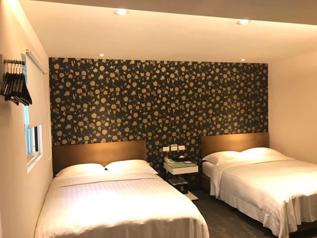 A hotel room with two beds, a nightstand, and a wall with a floral pattern.
