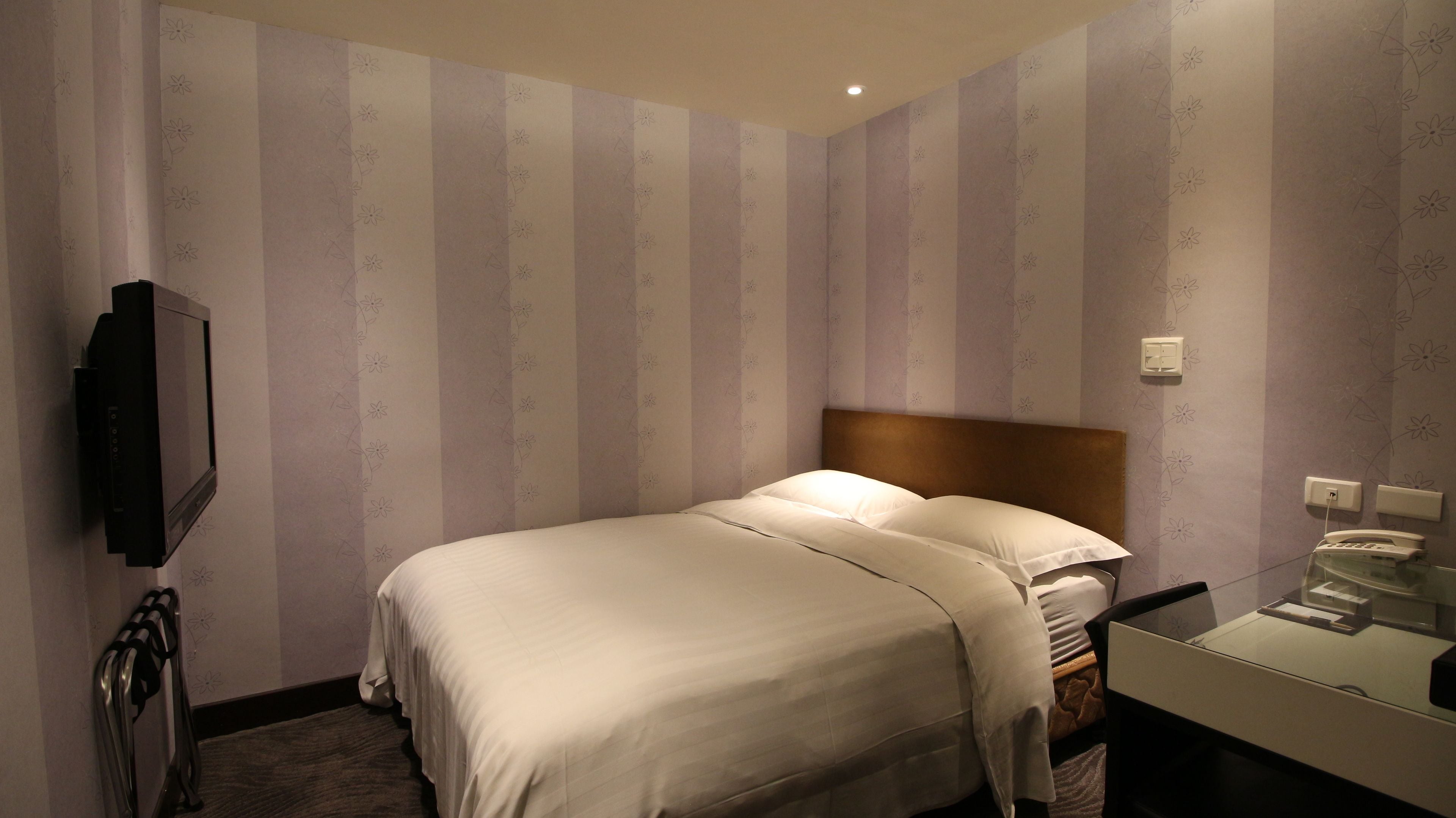 A hotel room with a bed, a TV, a bedside table, and a mirror.
