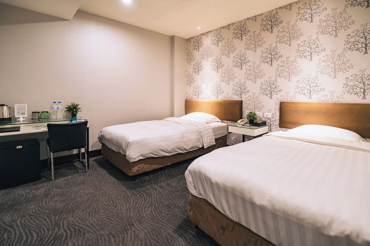 A hotel room with two beds, a desk, a chair, and a patterned wallpaper.