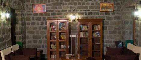 A cozy room with a stone wall, two wooden bookshelves, a round wooden table, and two wicker armchairs.