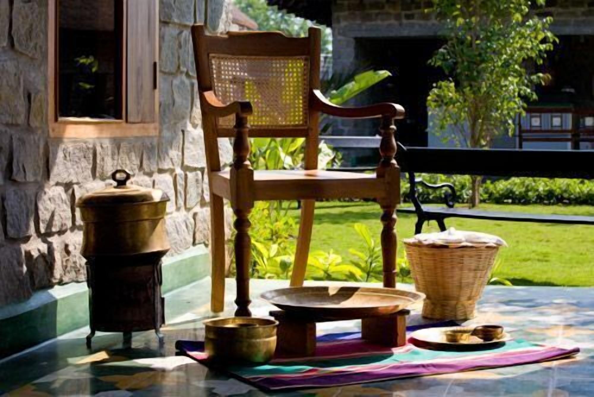 A wooden chair with a woven backrest, a metal pot, a small bowl, a woven basket, and a tray with a cloth on a tiled floor.