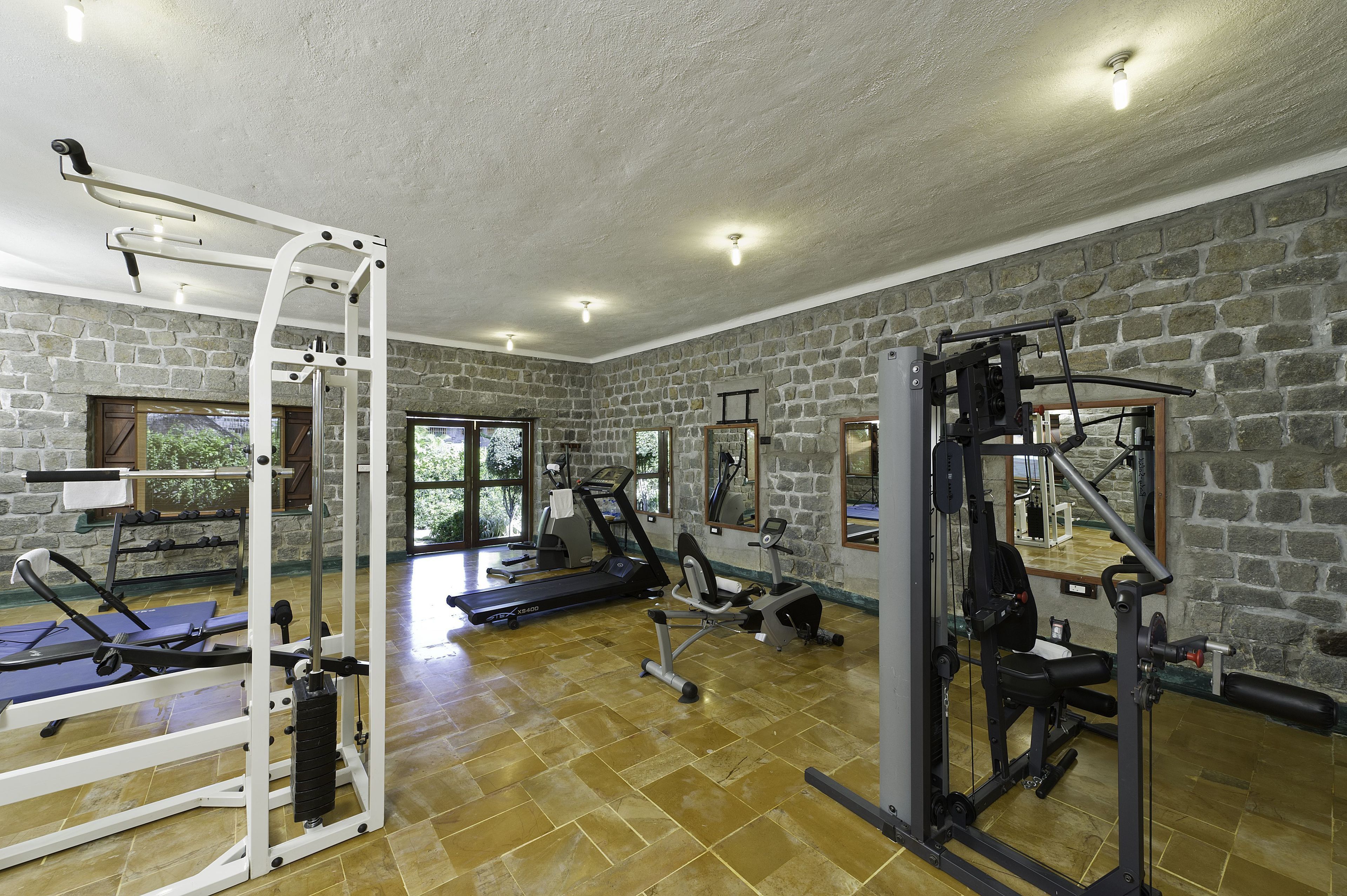 Et fitnessrum med stenvægge, træningsudstyr og store vinduer.