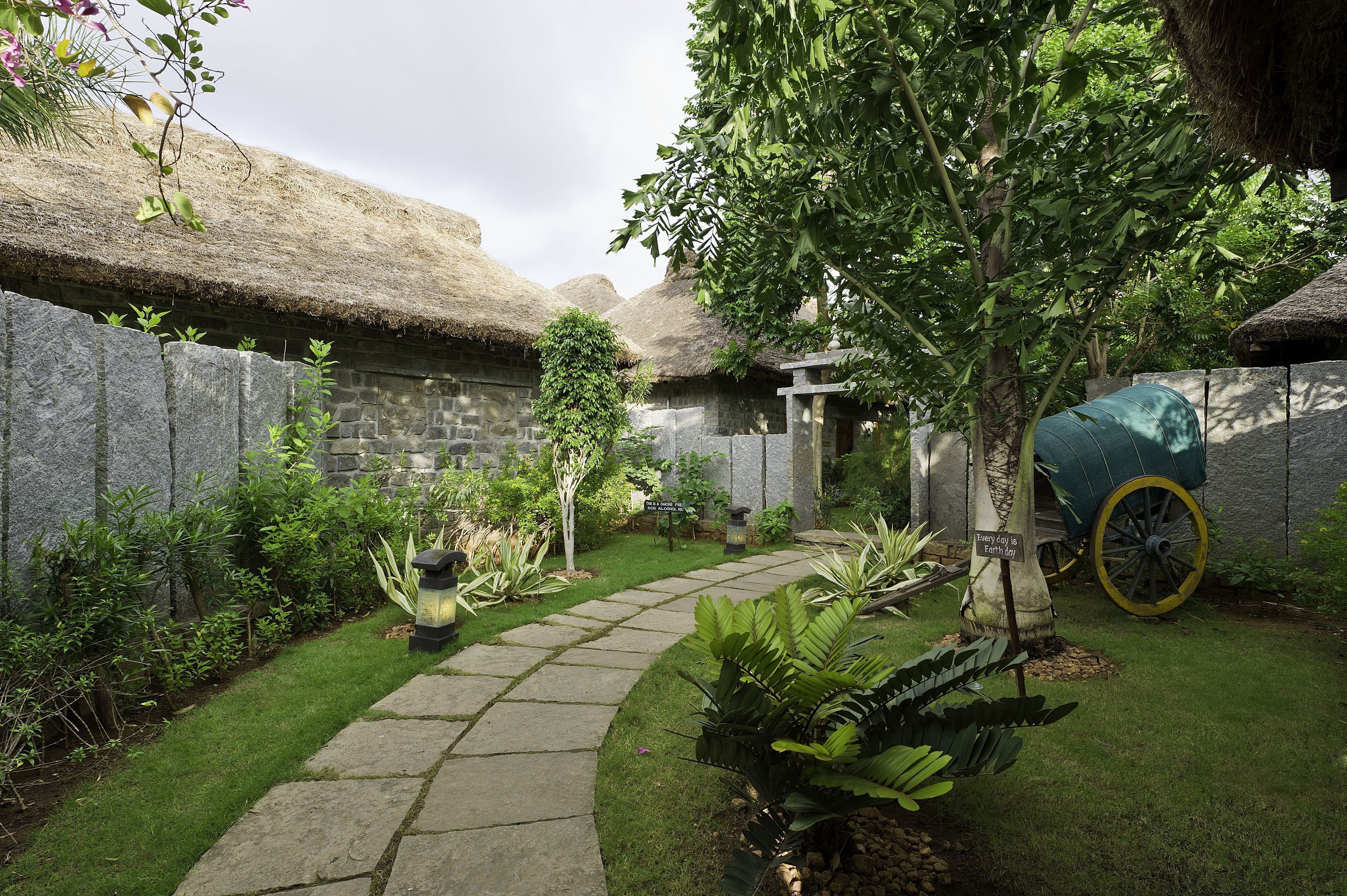 A garden with a stone pathway, a tree, and a thatched-roof structure.