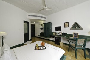 Habitación de hotel con cama, escritorio, silla, pequeño armario, televisión y estante en la pared.
