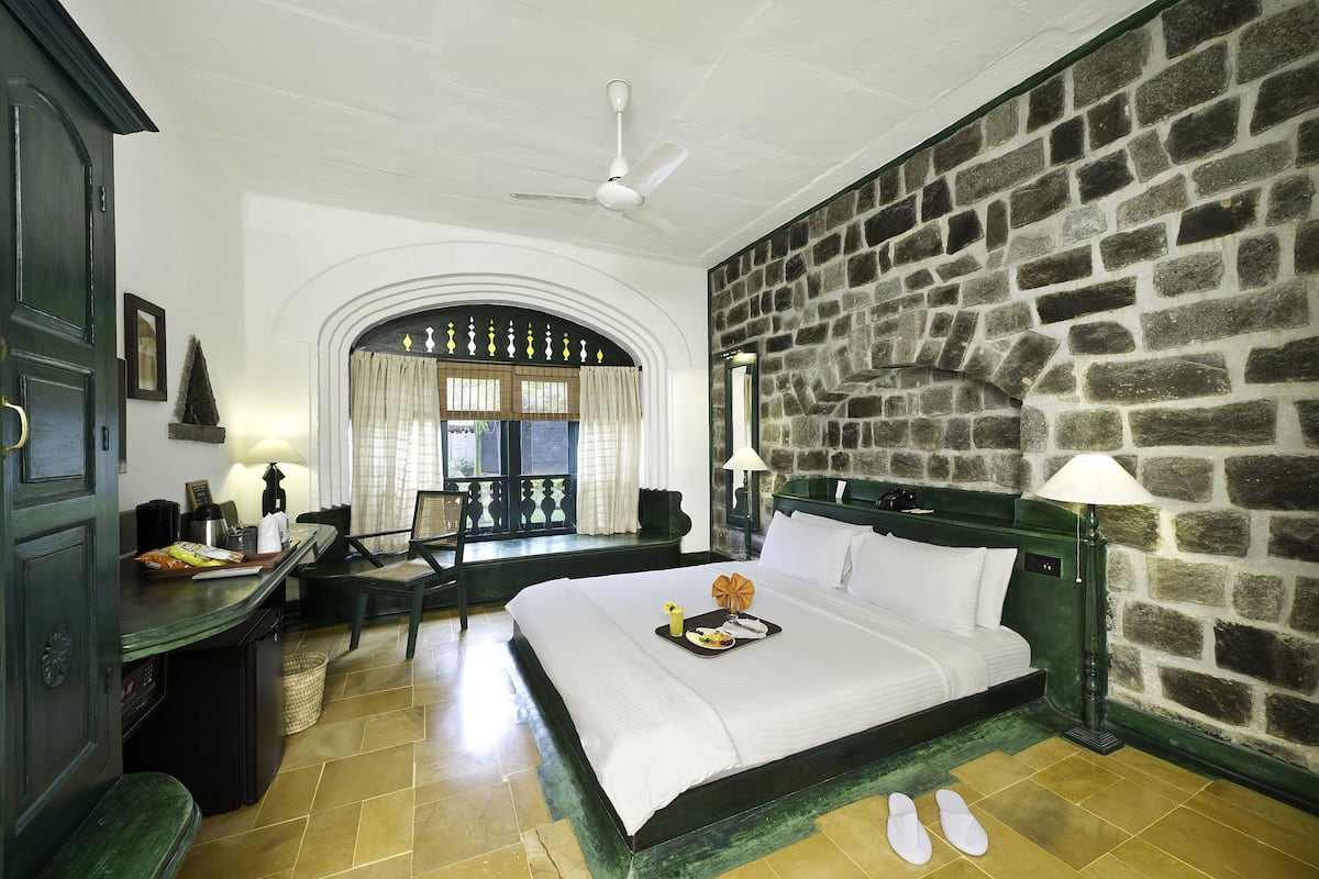 Habitación de hotel con pared de piedra, cama con ropa blanca, escritorio con lámpara y una silla.