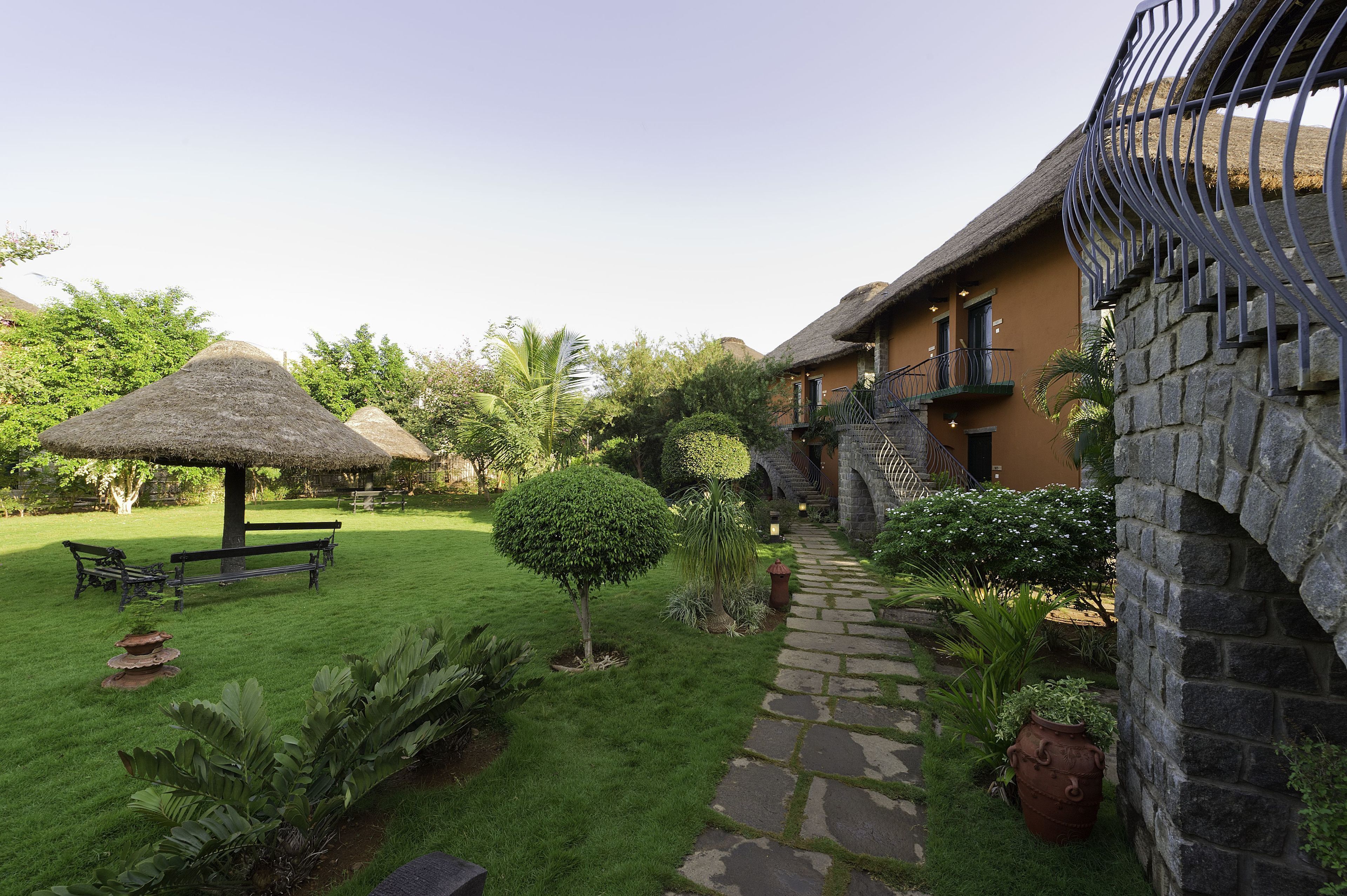 A courtyard with a thatched-roof gazebo, a stone pathway, and a small tree.