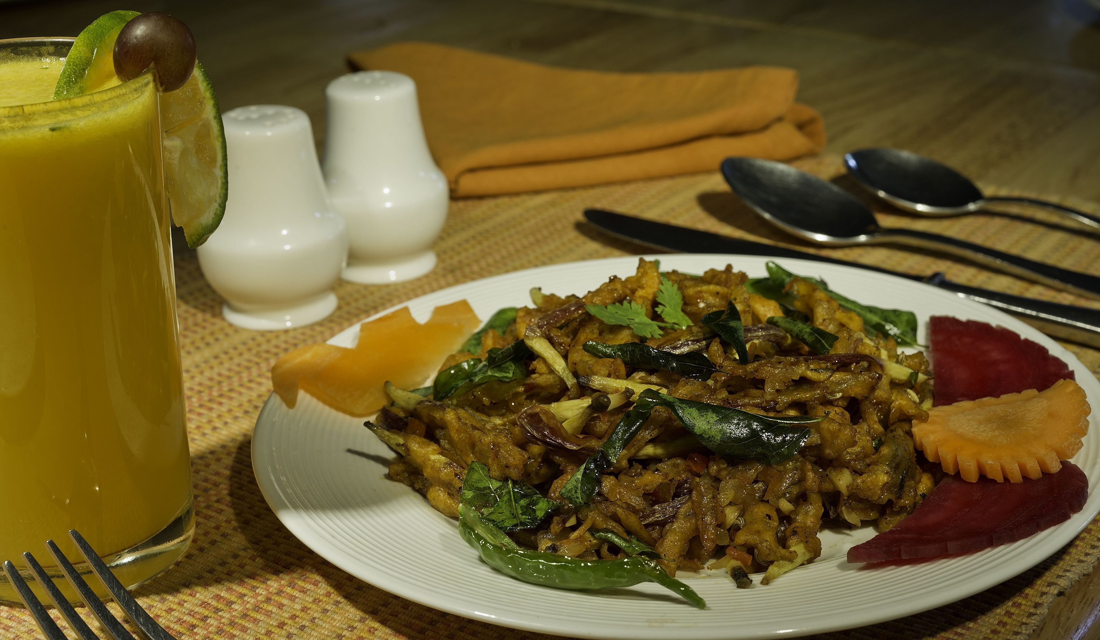 A plate of food with a lime wedge, salt and pepper shakers, and a fork on a table.