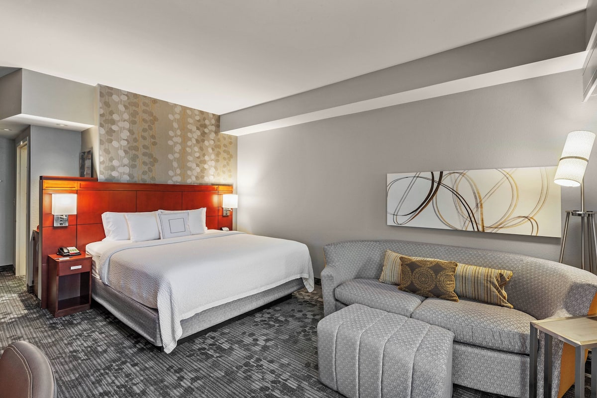 Una moderna camera d'albergo con un letto grande, un divano, un comodino e una lampada a parete.