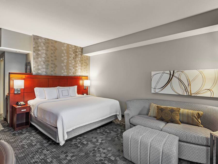 Una habitación de hotel moderna con una cama grande, un sofá, una mesita de noche y una lámpara de pared.