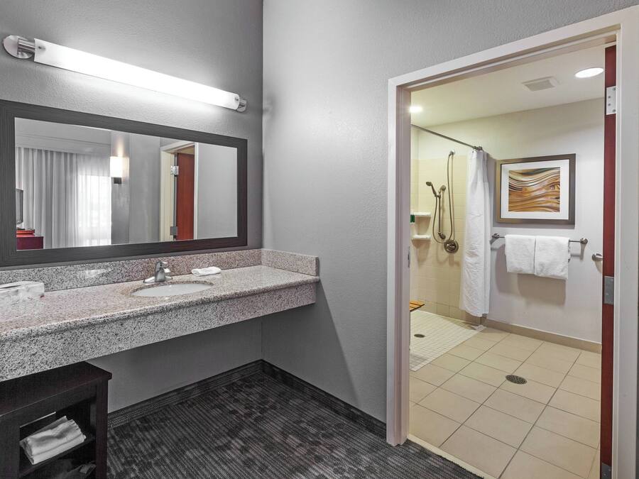 A modern bathroom with a granite countertop sink, a large mirror, and a shower area visible through an open door.