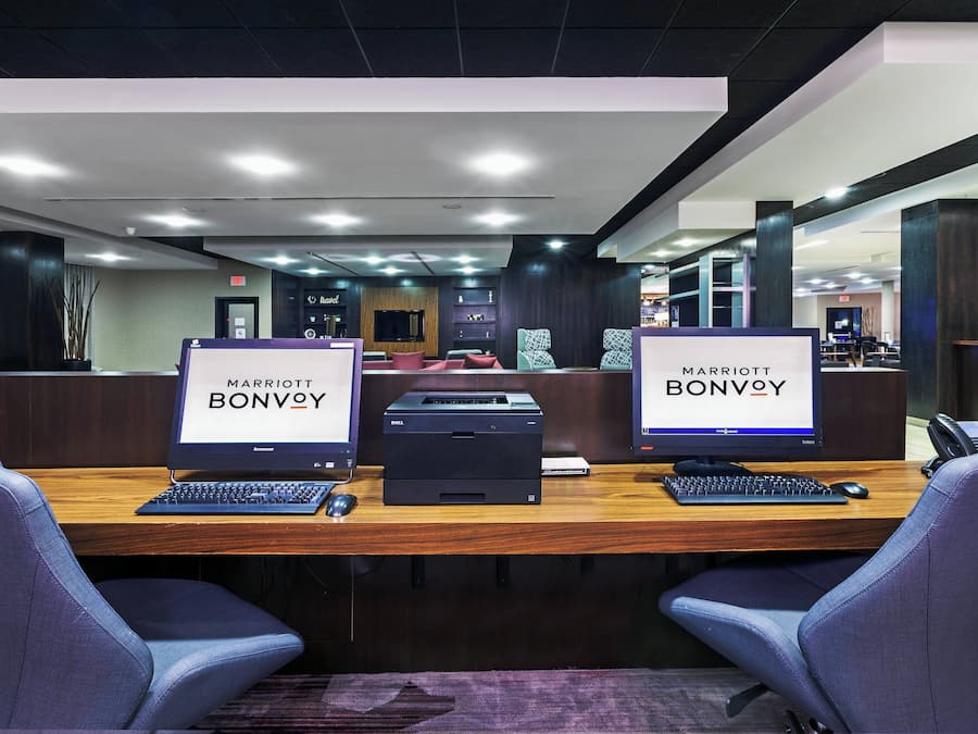 A hotel reception desk with two monitors displaying the hotel's name, a printer, and a telephone.