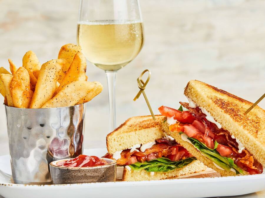 Un sandwich au bacon, à la tomate et à la laitue, un verre de vin blanc et une portion de frites.