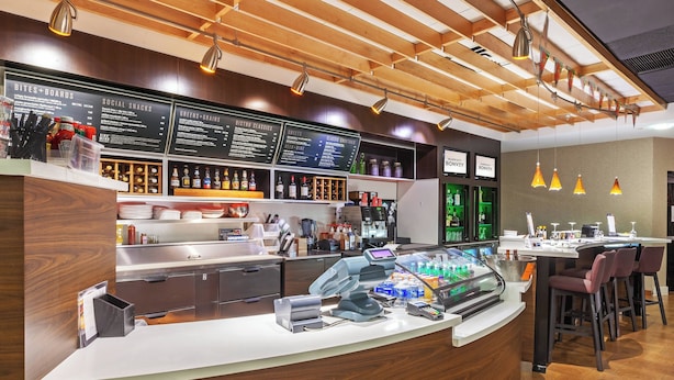 Un espace bar moderne avec un comptoir en bois, des panneaux d’affichage pour le menu et des tabourets de bar.