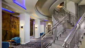 A modern hotel lobby with a curved staircase, seating area, and patterned carpet.