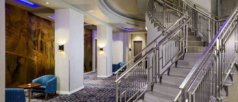 A modern hotel lobby with a curved staircase, seating area, and patterned carpet.