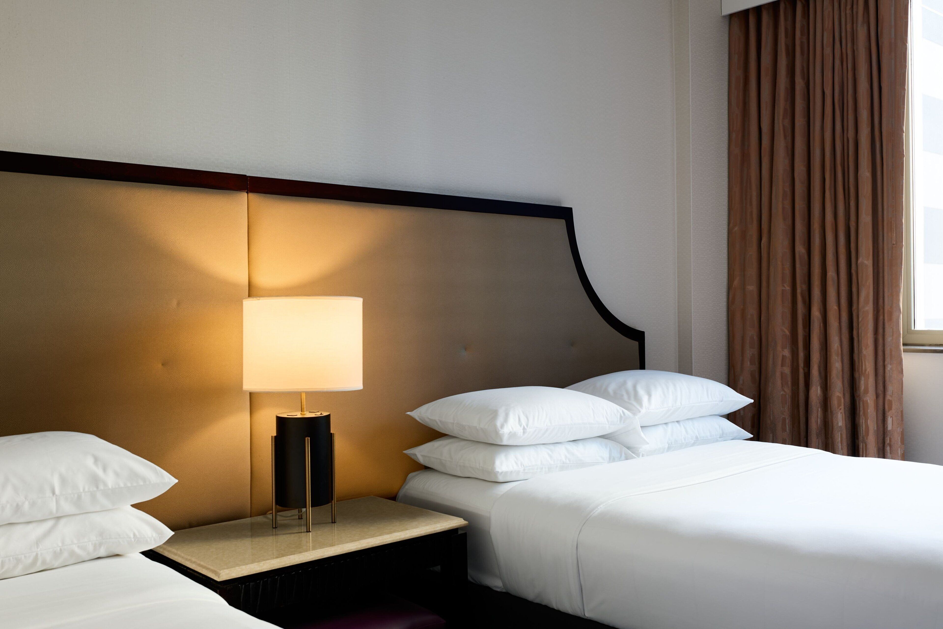 Ein Hotelzimmer mit einem Bett, einem Nachttisch mit Lampe und einem Fenster mit Vorhängen.
