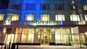 A Sheraton hotel with a modern glass facade, illuminated entrance, and visible American flag.