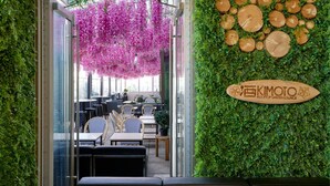A rooftop garden lounge with indoor seating, hanging pink flowers, and a wooden sign.