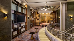 A modern hotel lobby with a curved seating area, a large flat-screen TV, and a patterned carpet.