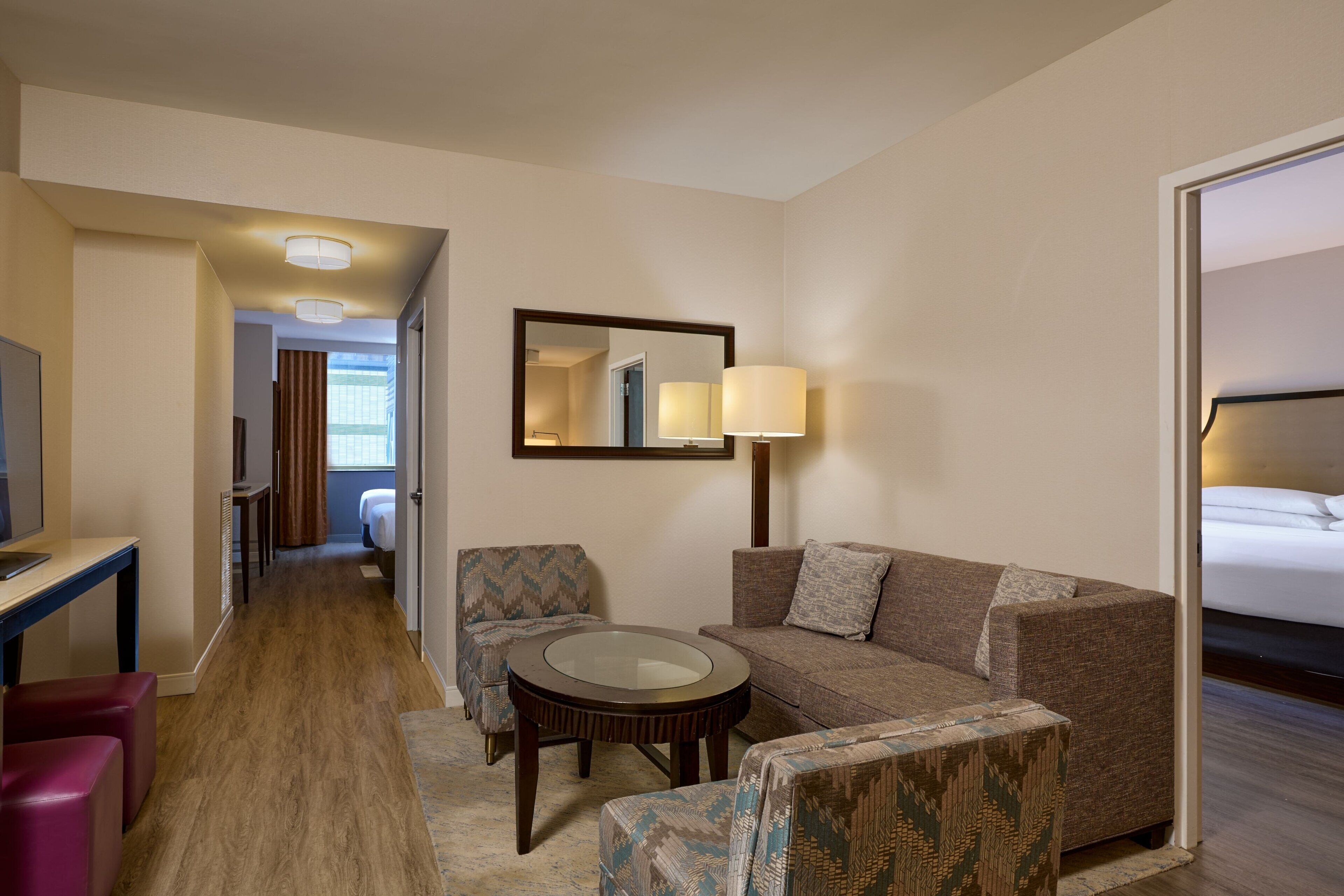 Une chambre d’hôtel avec un canapé, un fauteuil, une petite table ronde et un téléviseur.